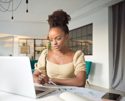 A woman sits at a desk and works at her laptop