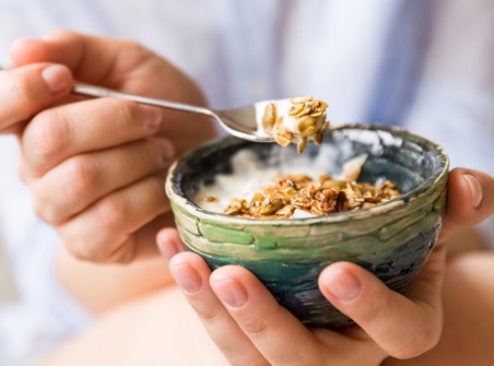 Hands holding a bowl of yogurt topped with granola