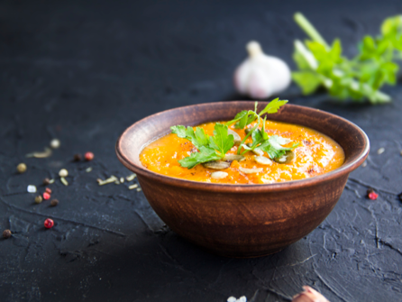 Bowl of orange curry garnished with a swirl of yogurt and fresh herbs