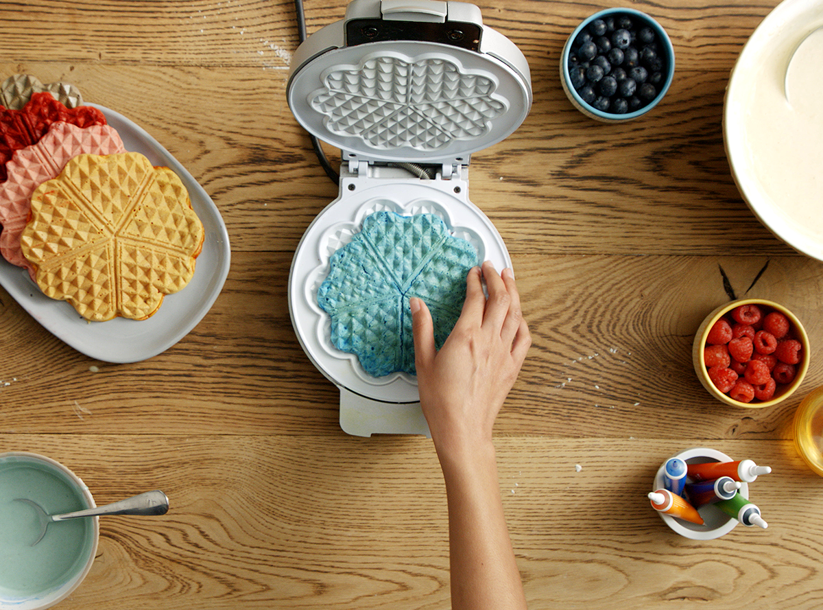 A hand removing a blue waffle from a waffle maker