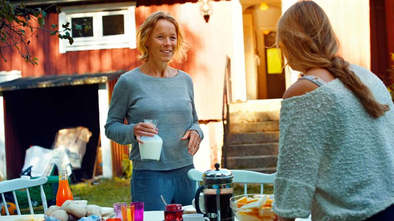 A mother holding a jar of milk in front of her teenager in a garden