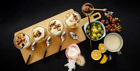 Table with a wooden platter containing olives, dips, lemon, and various other snacks