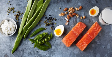 Assorted high-protein foods including salmon, eggs, and vegetables arranged on a table