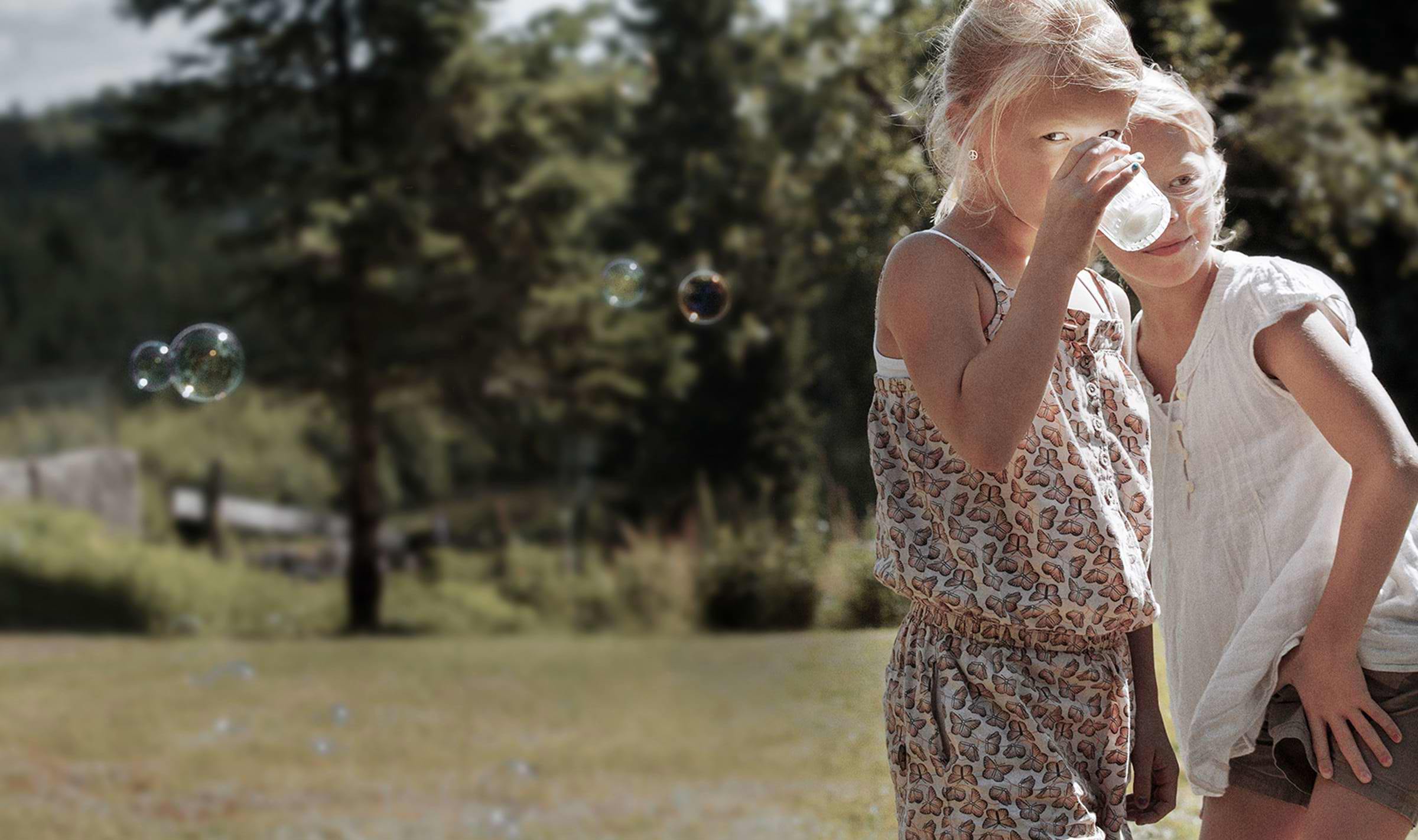 A pair of girls, one of whom is drinking a glass of milk